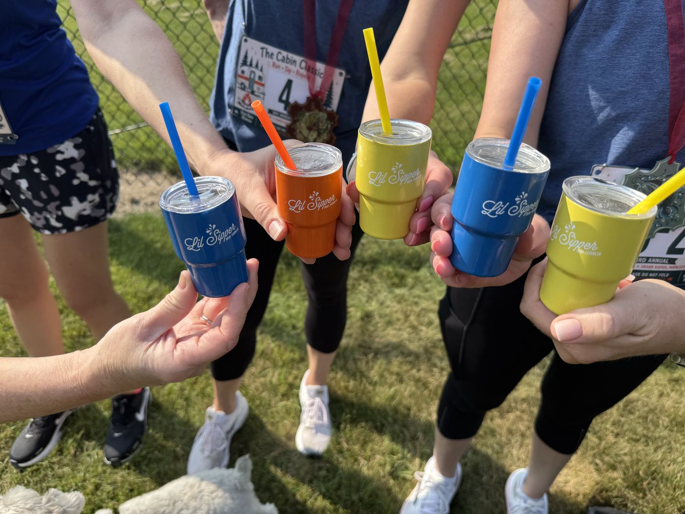 Five insulated tumblers raised in a toast on the grass after the race